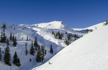 Winter mountain landscape with lots of fresh snow and a lonely peak on the background in clear winter day