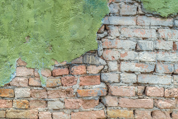 green plaster has cracked to reveal a worn brick wall