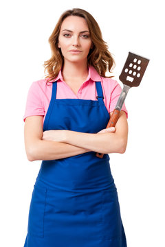 Pretty Blond Woman Wife Mother Girlfriend Bbq Grill Chef In Blue Apron With Arms Crossed Clutching Barbecue Spatula Isolated On White Background