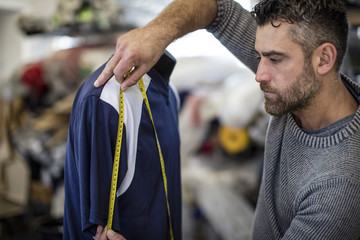 Tailor measuring sports shirt on mannequin in workshop