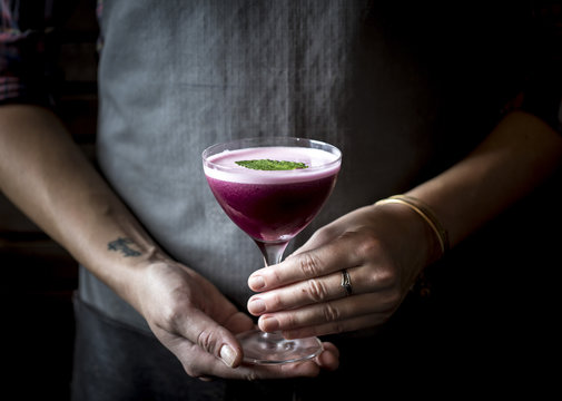 Woman holding blueberry cocktail in coupe glass