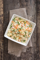 Russian salad in white bowl on rustic wooden

