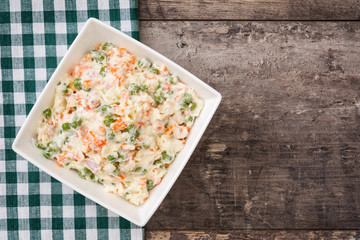 Russian salad in white bowl on rustic wooden

