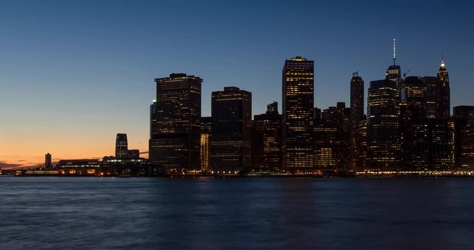 New York City Lower Manhattan skyscrapers from sunset to dusk through nightfall with city lights. Time lapse cityscape view of the Financial District and East River