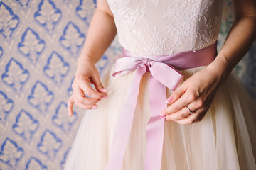 Closeup of a young caucasian girl tying a bow on her lace wedding dress. Shallow focus.