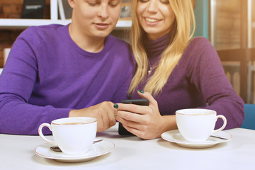 Young man and woman looking at the phone, read SMS or watch photos.