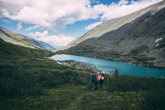 Travelers with backpacks come down to the mountain lake across the bushes