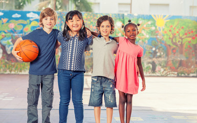 Happy mixed race primary classroom embracing in schoolyard. Inte
