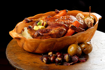 Roasted duck with golden crispy skin served with baked apples and chestnuts. Served on a ceramic blowl over rustic dark wooden table