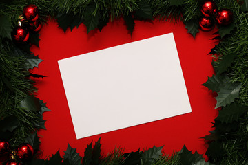 Fototapeta na wymiar White sheet of paper in a frame of branches of Christmas tree and red balls on a red background