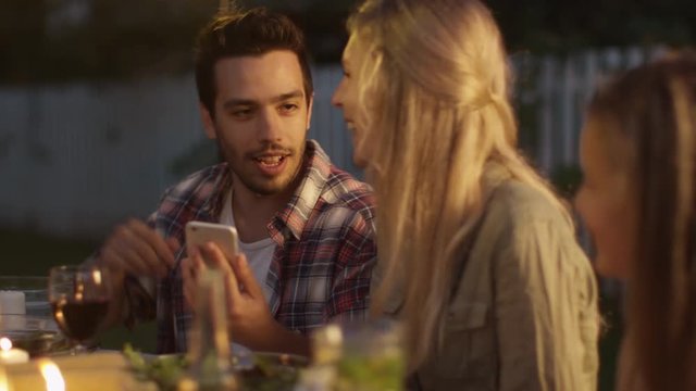 Handsome Man Using Mobile Phone and Showing Content to His Girlfriend during Family Dinner.