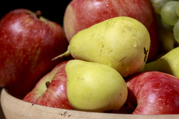 Delicious pears beside red apples and other fruits, into ceramic bowl