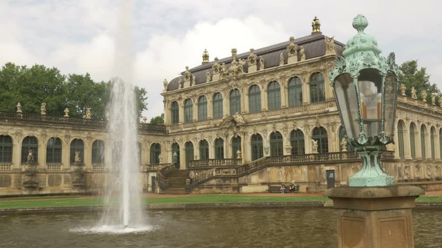 Static shot of one of the main fountains of Zwinger Palace with tourists. An ornate lamp frames the shot