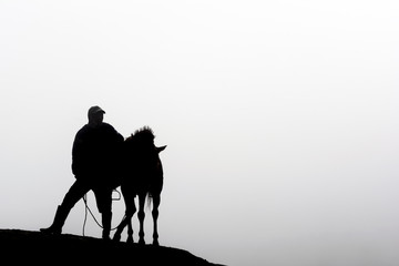 Obraz na płótnie Canvas Silhouette of a horsemen resting on the sand dune with foggy / misty morning background at Bromo-Tengger-Semeru National Park, East Java, Indonesia