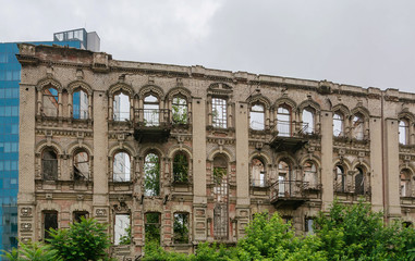 Abandoned damaged old house with blank windows against blue cloudy sky