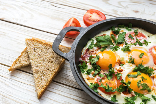 Pan of fried eggs, tomatoes and parsley with bread