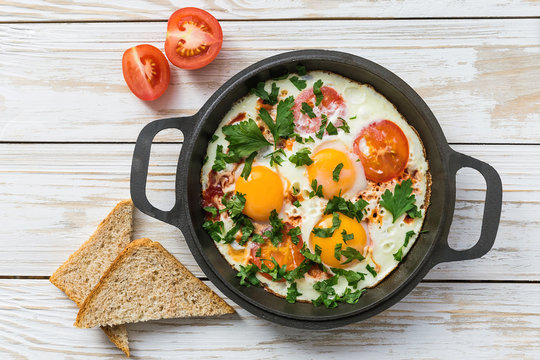 Pan of fried eggs, tomatoes and parsley with bread
