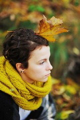 Portrait of young attractive girl in a knit scarf with a maple leaf in her hair in the autumn forest, side view.