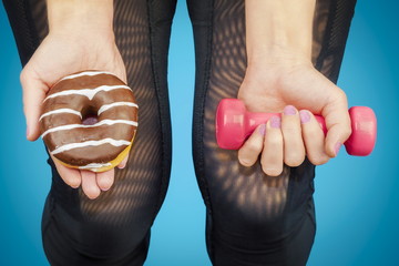 Woman with dumbbell and donut in the hands of - obrazy, fototapety, plakaty