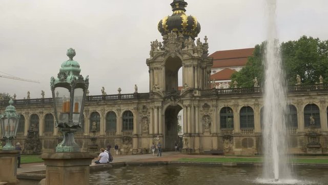 Tilt shot of one of the main fountains of Zwinger Palace with tourists. An ornate lamp frames the shot
