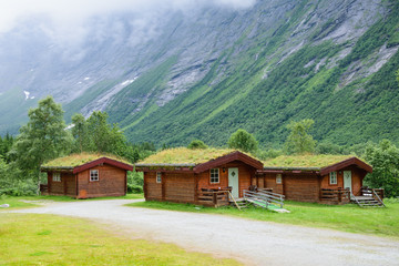 Fototapeta na wymiar Norwegian wooden houses with grass on the roof at the foot of the mountain