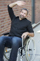 Fototapeta na wymiar man in wheelchair waving to somebody and smiles