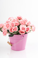 Romantic decor of pink and white, yellow, cream rose flower bouquet in the pink and blue iron (metal) bucket/container. Isolated background.  Greeting card with artificial flowers.