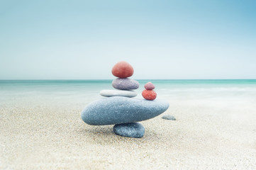 Balancing colorful zen stones pyramid on sandy beach under blue sky. Beautiful nature and spiritual concept