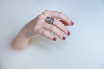 A girl's hand protruding from a bath of water and milk in a bathtub. The rest of the body is submerged. 