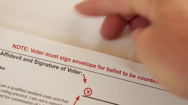 A man's hands slide a mail in ballot into an official envelope for the 2016 election.