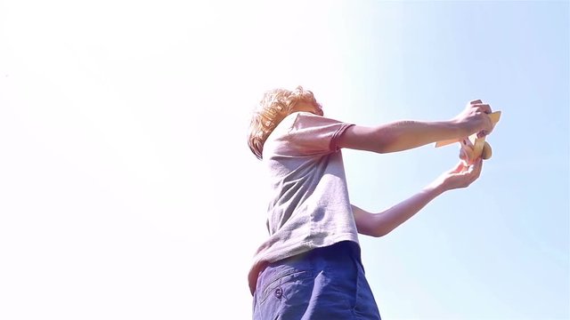 Low angle shot of a boy playing with wooden toy airplane against blue sky, slow motion