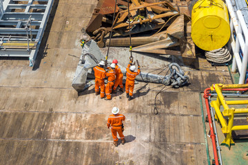 Offshore crews handling and lifting anchor for deployment on construction barge