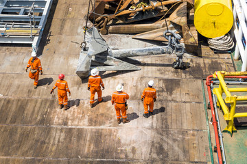 Offshore crews handling and lifting anchor for deployment on construction barge