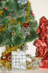 Fototapeta na wymiar Christmas tree decorated with bright colorful toys, snowflakes. Under the tree are gifts of silver and gold gift bags and gift in a red-golden shiny packaging
