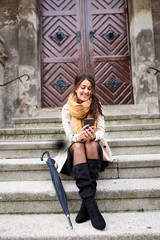 Woman with black umbrella sitting on the stairs in the old town and looking at mobile phone.