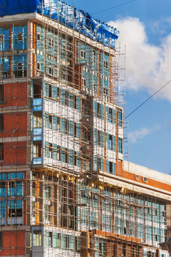 Construction of a building. A brick wall surrounded by scaffolding.
