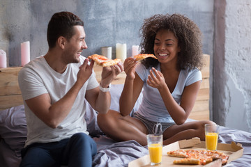 Happy couple eating pizza in bed
