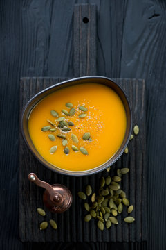 Black wooden serving board with pumpkin cream-soup in a bowl