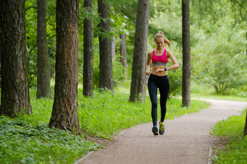 Young slim woman jogging in a park looking to smart watch