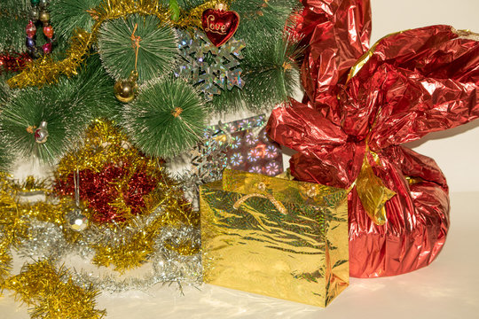 Christmas tree decorated with bright colorful toys, snowflakes. Under the tree are gifts of silver and gold gift bags and gift in a red-golden shiny packaging