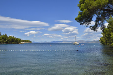 Fototapeta na wymiar Bay in adriatic sea on Brac Island in Croatia with clear water and blue sky and a boat in background.