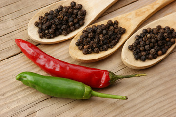 Black and red pepper in wooden spoon on the old board