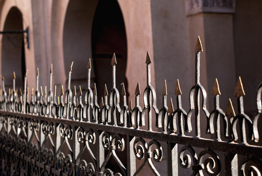 A metal railing with sharp pointed edges on top and a building with arched doorways