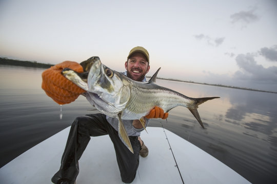 A man proudly holds a large fresh caught fish on the stern of a boat;Puerto rico
