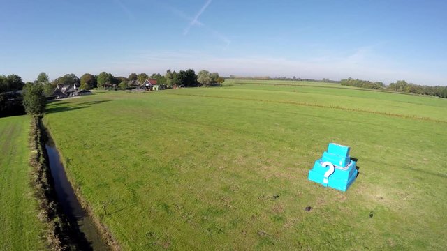 Aerial of white question mark on small bright blue structure drone flying towards cube with ?  also showing quadcopter shadow blue sky background footage could indicate FAA drone regulations 4k