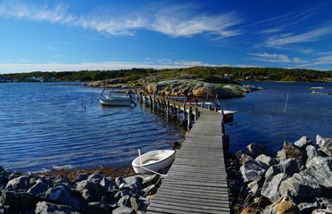 Wooden pier with small, moored ships between bare rocks on the seaside of Donsö, an island of the archipelago of Gothenburg (Göteborgs skärgård), Sweden