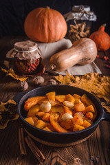 Autumn composition with roast pumpkin and garlic in a cast iron skillet on a wooden table with maple leaves, dried mushrooms, rosehips and whole pumpkins. Photos in rustic style.