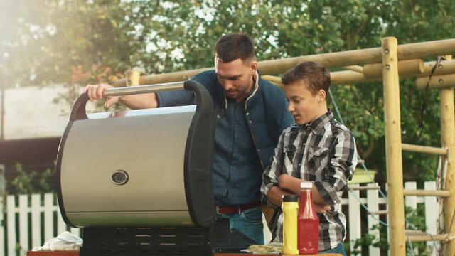 Father and Son Are Cooking Burgers on Grill at Bright Summer Day.