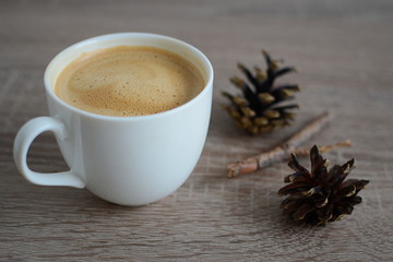 Cup of coffee and pine cones on wooden table
