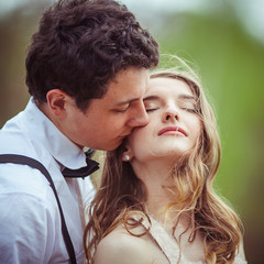 Tender man kisses woman's peach cheek while wind blows her hair